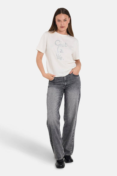 Jean droit en denim gris foncé de FREEQUENT, porté avec un t-shirt blanc à motif.
