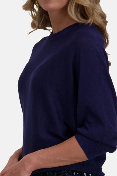 Pull bleu à col rond de FREEQUENT, porté avec un bas à paillettes et des boucles d'oreilles dorées.