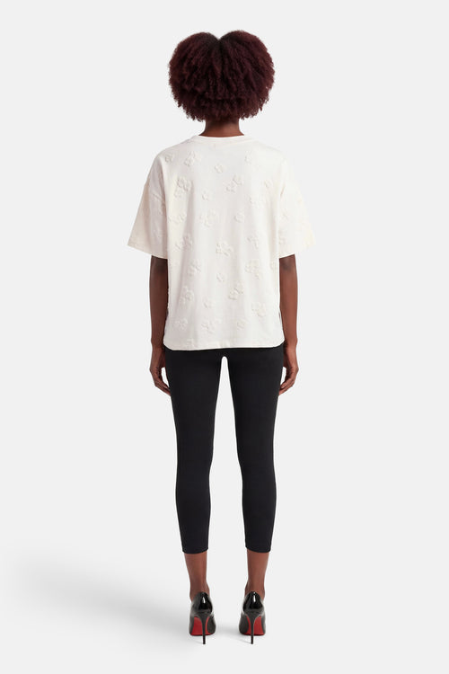 T-shirt blanc à manches courtes de FREEQUENT, motif fleuri en relief, porté avec un legging noir et des escarpins vernis.