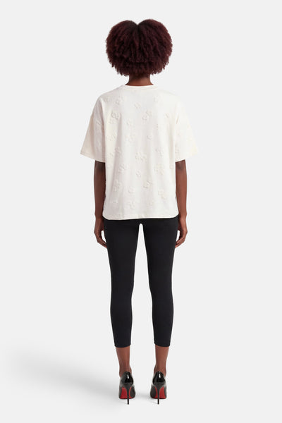 T-shirt blanc à manches courtes de FREEQUENT, motif fleuri en relief, porté avec un legging noir et des escarpins vernis.