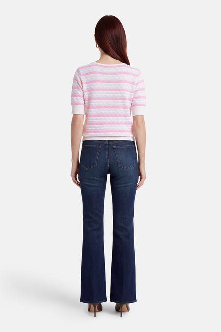 Pull multicolore par FREEQUENT, rayé rose et blanc, porté avec un jean bleu foncé évasé et des chaussures marron à talons aiguilles.
