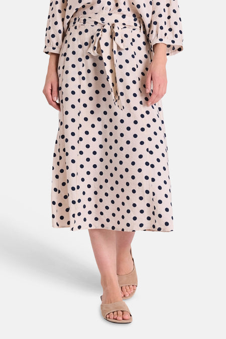 Jupe midi beige à pois bleu marine de FREEQUENT, portée avec une ceinture à la taille et des sandales.