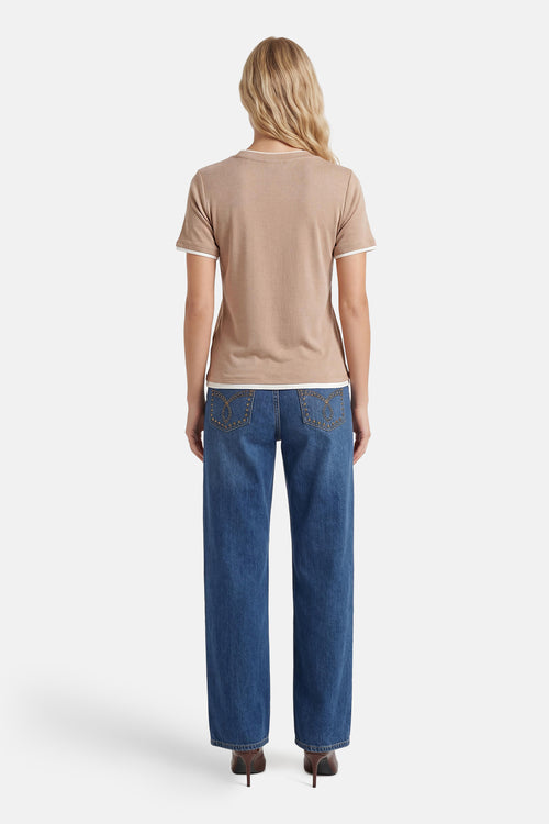 T-shirt à manches courtes beige de FREEQUENT, avec finitions blanches, porté avec un jean bleu et des talons marron.