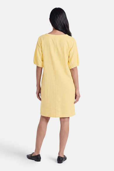 Robe jaune de FREEQUENT, vue de dos, manches bouffantes, en tissu texturé, portée avec des chaussures plates noires.