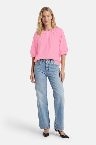 Blouse rose à manches 3/4 de FREEQUENT avec encolure froncée et fendue, portée avec un jean clair et des talons noirs.