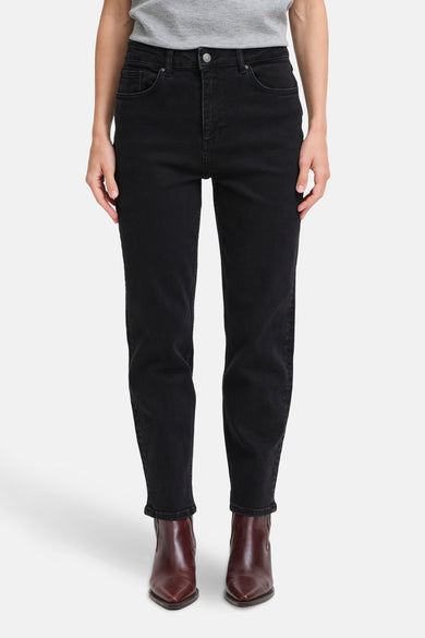 Jean Mom en denim noir de B.YOUNG, porté avec un t-shirt gris et des bottines marron pointues.

