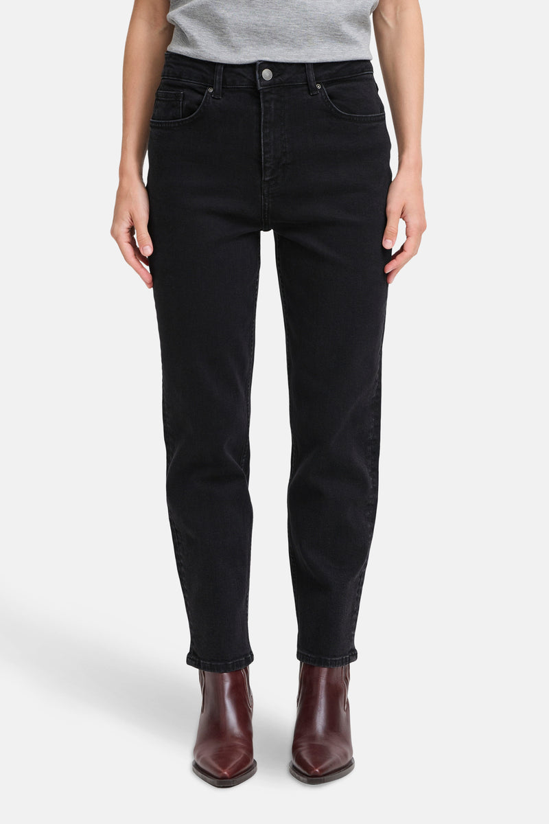 Jean Mom en denim noir de B.YOUNG, porté avec un t-shirt gris et des bottines marron pointues.
