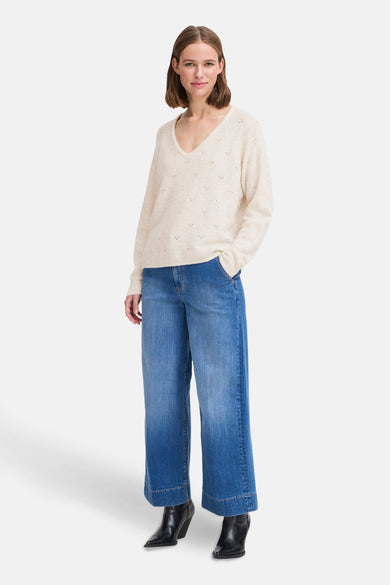 Pull écru à col en V par B.YOUNG, avec motifs ajourés sur toute la surface, porté avec un jean ample bleu et des bottines noires.