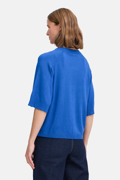 Pull à col rond bleu de B.YOUNG, manches courtes, porté avec un pantalon ample en denim foncé.
