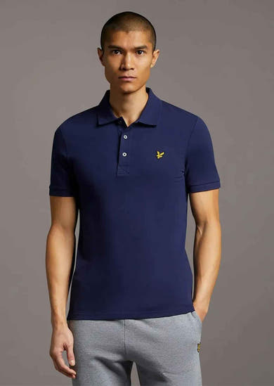 Polo bleu marine de LYLE & SCOTT avec logo brodé, porté avec un pantalon de survêtement gris.