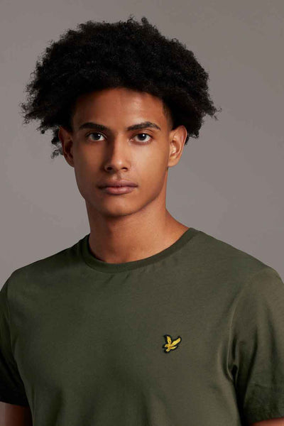 Olive green short-sleeve t-shirt with yellow bird embroidery on chest, worn by model in front view