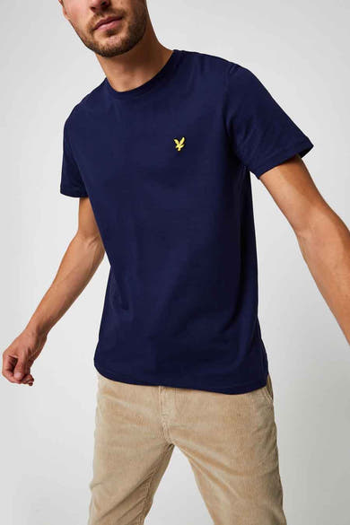 T-shirt bleu à manches courtes de LYLE & SCOTT, avec logo discret sur la poitrine, porté avec un pantalon en velours côtelé.
