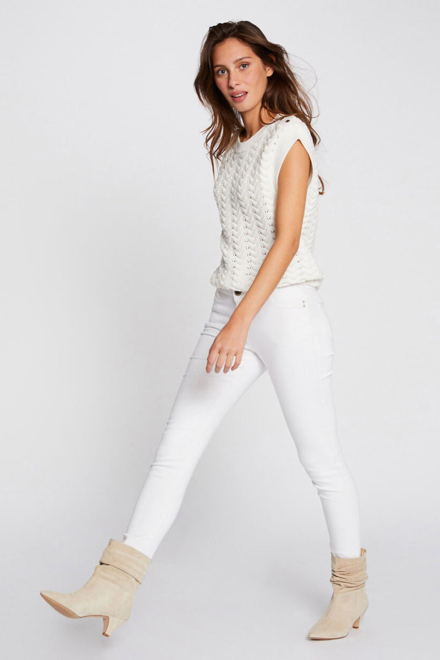 Pantalon blanc de Morgan de Toi, coupe skinny, porté avec un pull sans manches et des bottines en daim beige.
