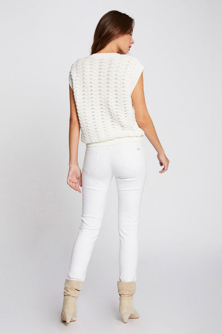 Pantalon blanc de Morgan de Toi, coupe slim, porté avec un pull sans manches en maille et des bottines en daim.