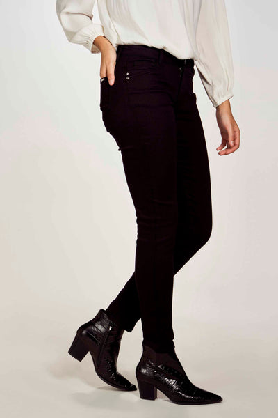 Pantalon noir de Morgan de Toi, coupe skinny, porté avec un chemisier clair et des bottines en cuir verni.
