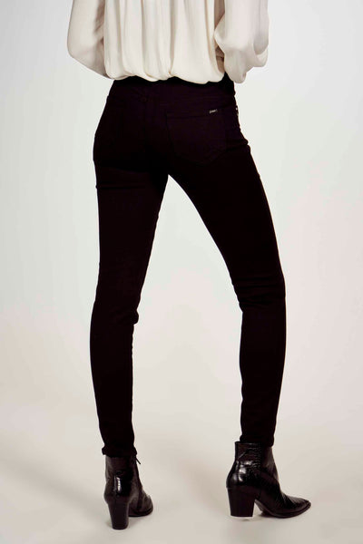 Pantalon noir de Morgan de Toi, coupe skinny, porté avec un chemisier blanc et des bottines en cuir noir à talons.
