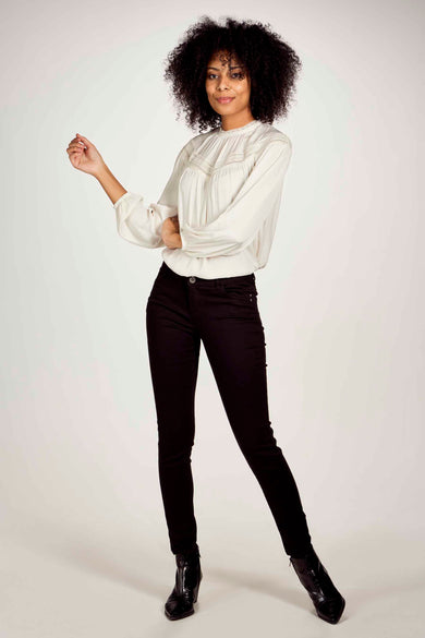 Pantalon noir de Morgan de Toi, coupe slim, porté avec un chemisier blanc et des bottines noires.