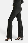 Black flared denim jeans by JADE, side view showing slim fit through thigh and wide leg opening, worn with black strappy heels