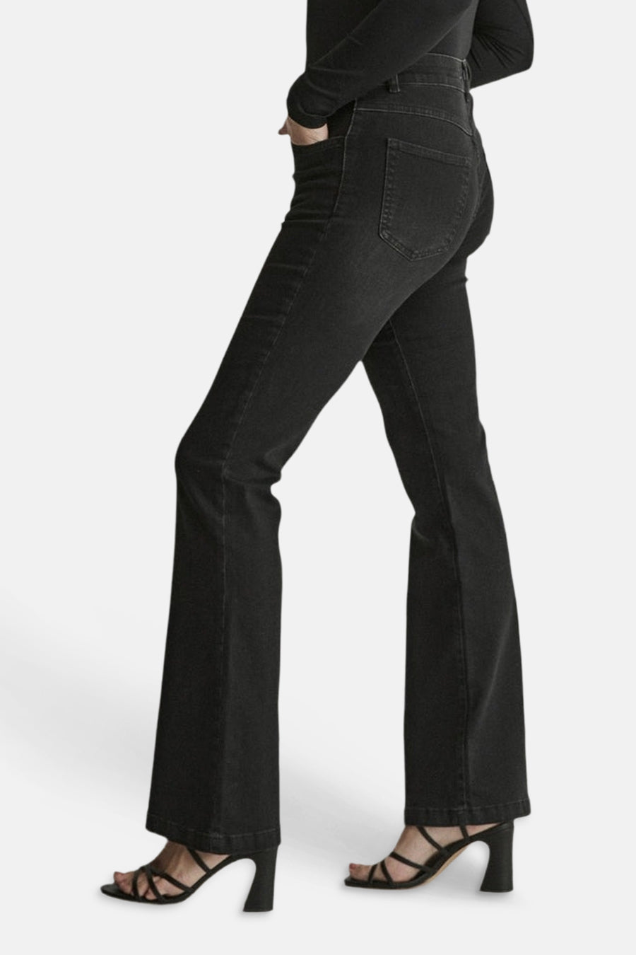 Black flared denim jeans by JADE, side view showing slim fit through thigh and wide leg opening, worn with black strappy heels