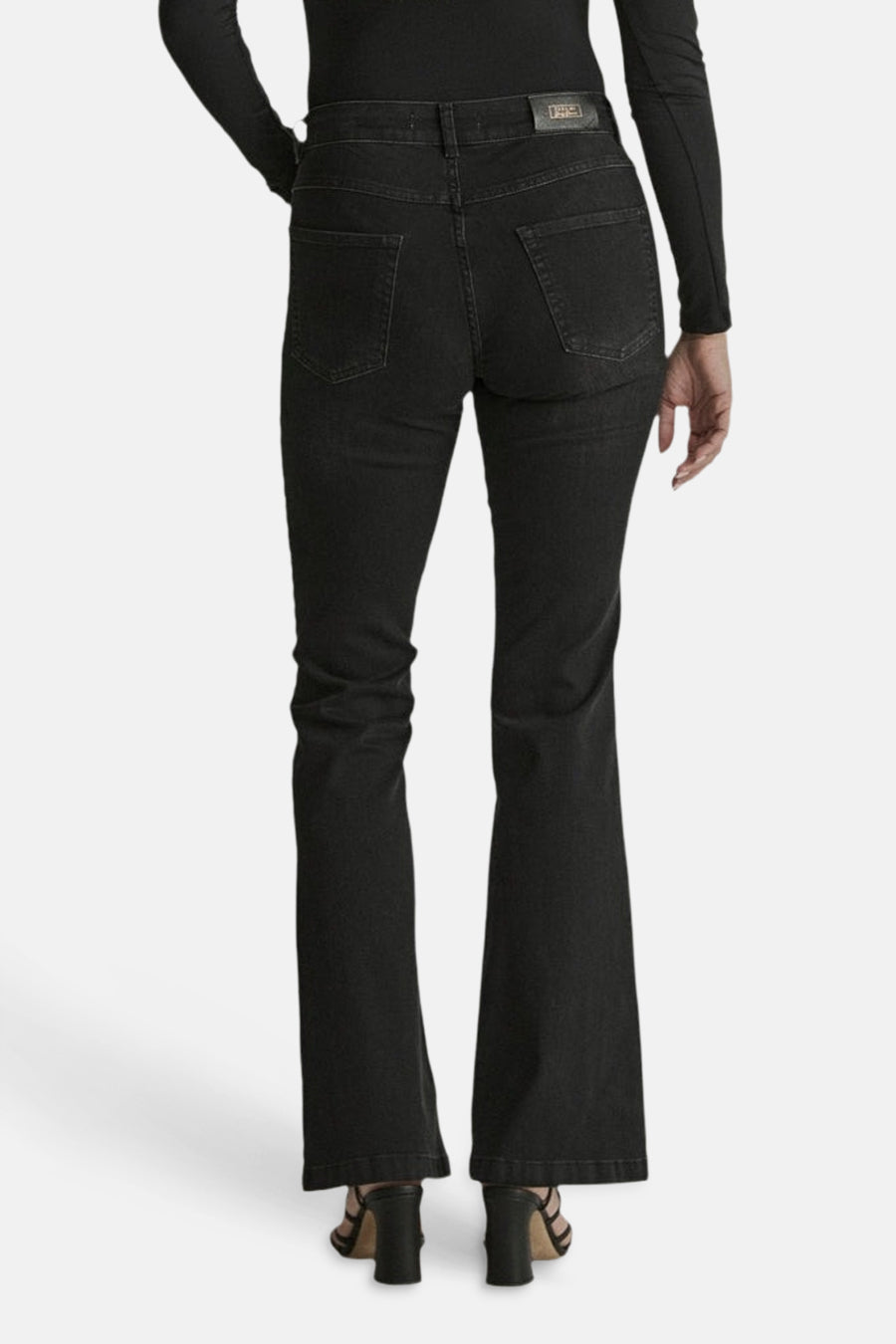 Black flared denim jeans by JADE, back view with classic stitching and straight-to-flare leg, worn with black top and heels