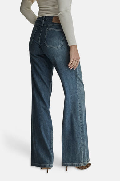 Light blue wide-leg denim jeans by MIRA, back view with classic stitching and flared hem, worn with beige top and leopard print heels