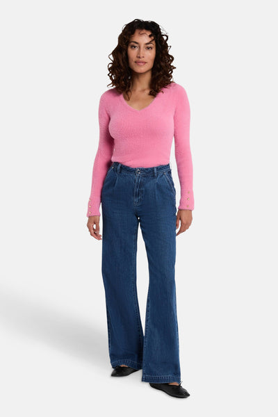 Roze V-hals trui van Morgan de Toi, met decoratieve knopen op de mouwen, gedragen met een wijde jeans.