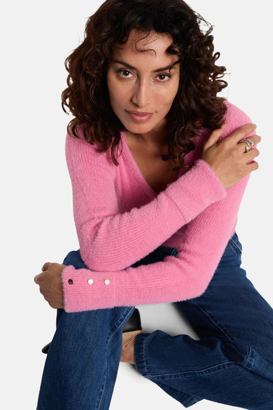 Roze V-hals trui van Morgan de Toi met lange mouwen en gouden knopen, gedragen met een donkere jeans.