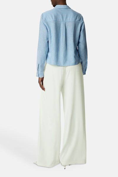 Chemisier bleu à rayures, à manches longues de COMMA, avec plis au dos, porté avec un pantalon blanc.
