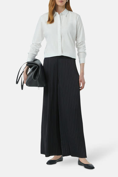Blauwe broek van COMMA, lang en geplooid, gedragen met een wit overhemd en zwarte ballerina's.