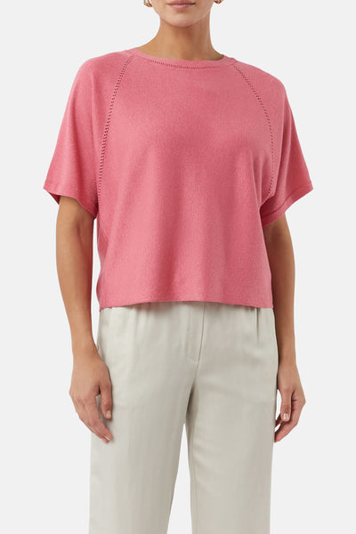 Pull à col rond rose COMMA, manches courtes avec détail ajouré, porté avec un pantalon beige uni.