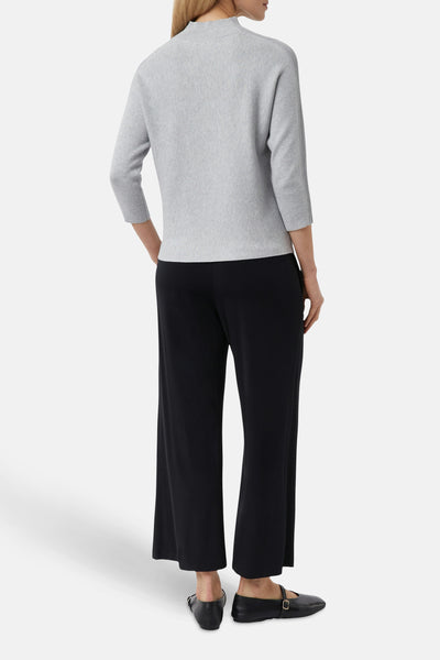 Pull gris de COMMA, coupe droite, manches trois quarts, porté avec un pantalon noir ample et des chaussures plates.