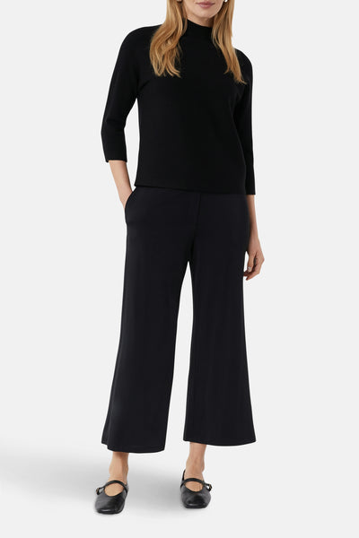 Pull noir de COMMA, avec manches trois quarts et porté avec un pantalon noir large et des ballerines.