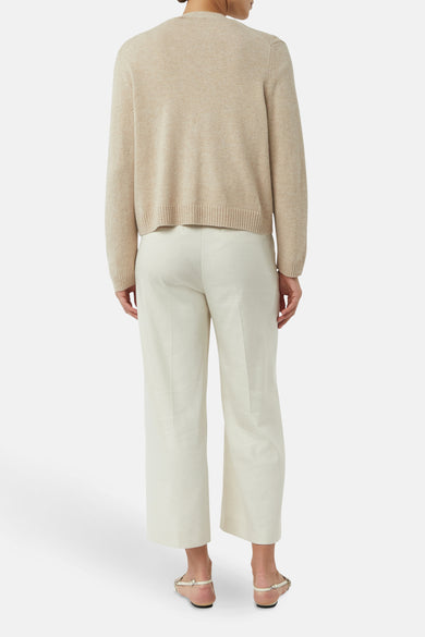 Cardigan beige de COMMA, porté avec un pantalon coupe droite couleur crème et des sandales.