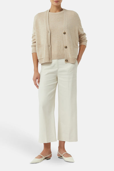Cardigan beige en tricot de COMMA, porté avec un pull ton sur ton et un pantalon blanc à jambes larges.