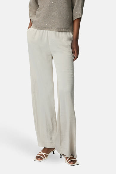 Pantalon écru de COMMA, coupe large et fluide, porté avec un haut beige à paillettes et des sandales blanches.

