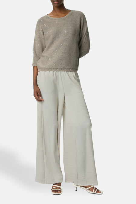 Ecru broek van COMMA, wijd en vloeiend, gedragen met een beige trui met pailletten en witte sandalen met hak.