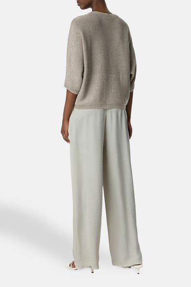 Pantalon écru de COMMA, large et fluide, porté avec un pull beige à paillettes.
