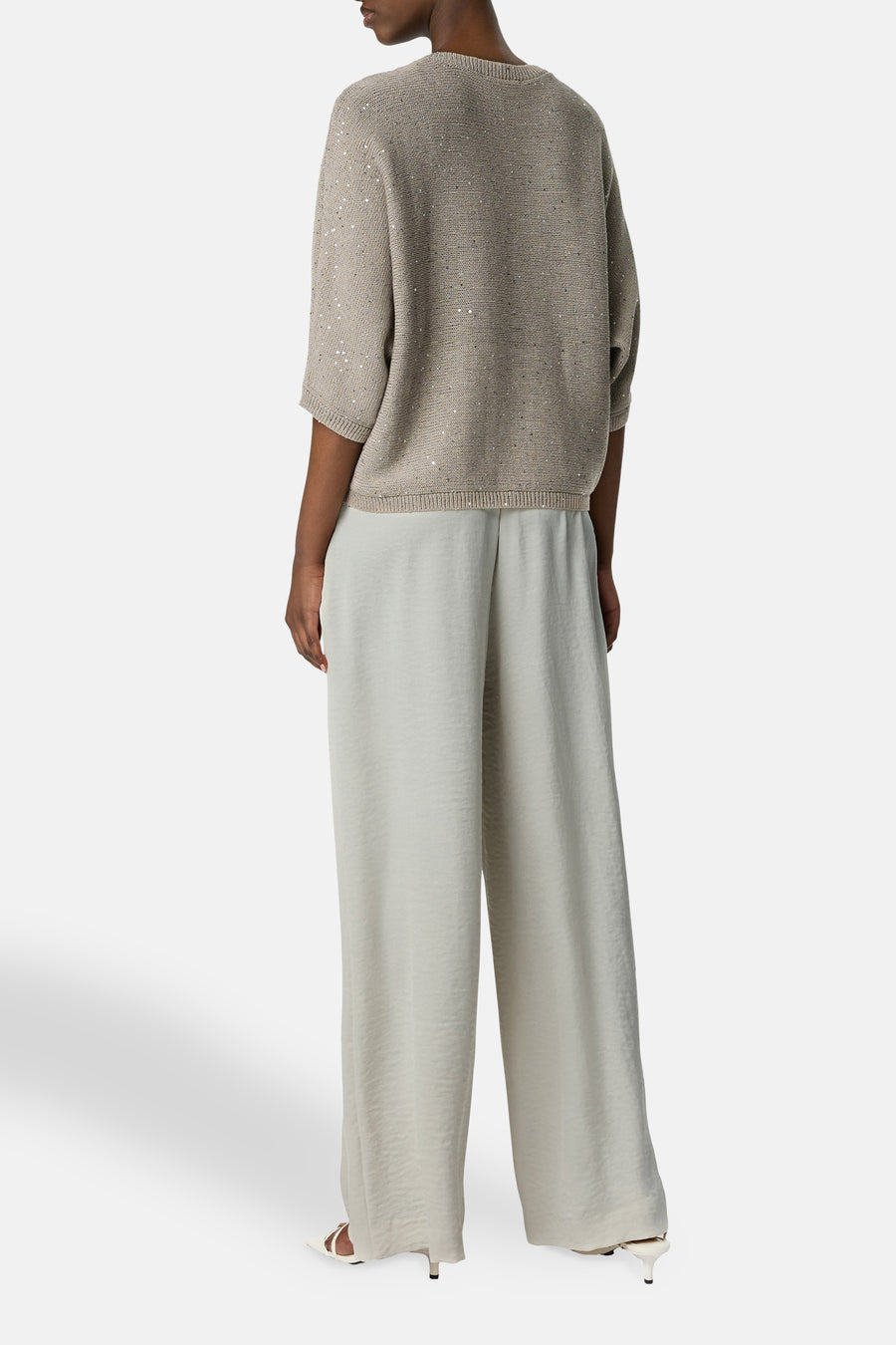 Pantalon écru de COMMA, large et fluide, porté avec un pull beige à paillettes.
