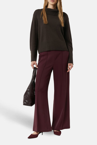 Bruine trui van COMMA, gedragen met een bordeauxrode broek met wijde pijpen en een leren handtas.