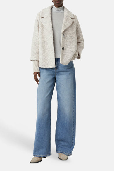 Korte beige jas van COMMA met bouclétextuur, gedragen over een coltrui en een wijde jeans.
