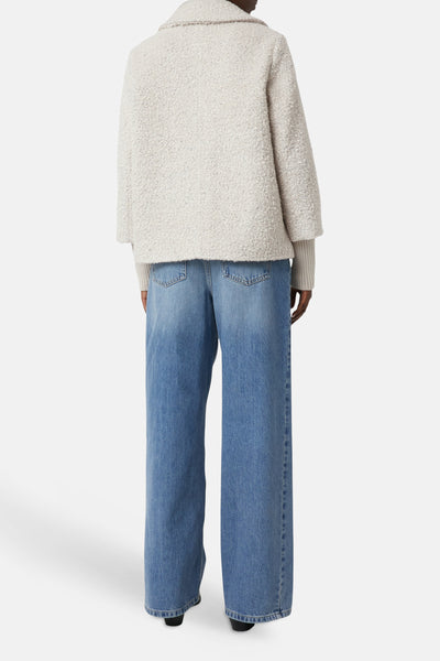 Korte beige jas van COMMA, getextureerd met kraag, gedragen met een trui en een wijde blauwe jeans, van achteren gezien.
