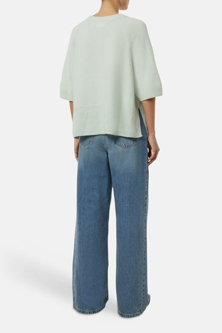 Pull col rond vert par COMMA, porté avec un jean ample bleu.