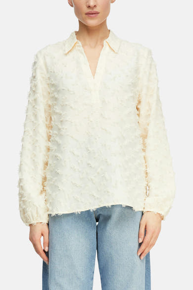 Blouse beige à manches longues de COMMA, avec texture en relief et col en V, portée avec un jean bleu.
