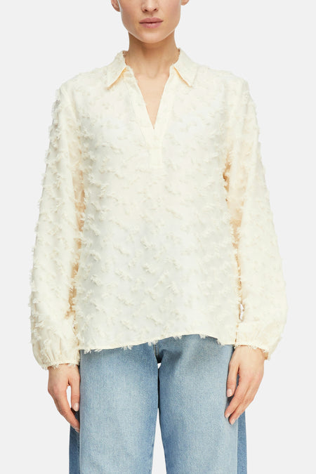 Blouse beige à manches longues de COMMA, avec texture en relief et col en V, portée avec un jean bleu.
