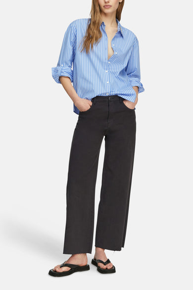 Chemise bleue à rayures blanches de COMMA, portée déboutonnée avec un pantalon noir large et des tongs.