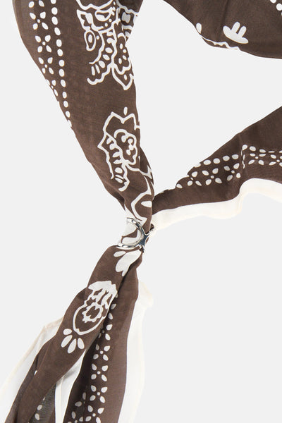 Brown foulard with white floral and dot patterns, tied with silver ring, close-up view
