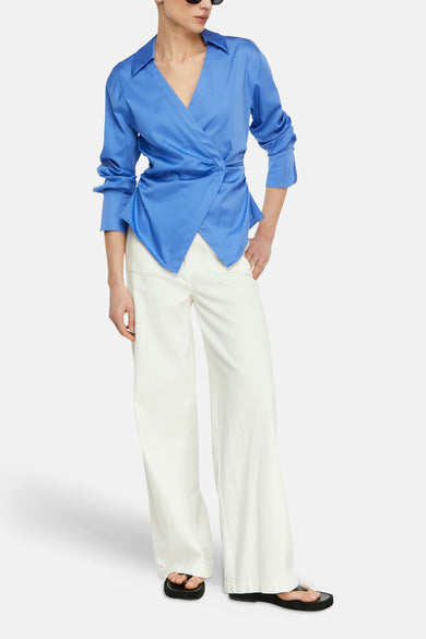 Blauw overhemd met lange mouwen van COMMA, met een overslag aan de voorkant en een asymmetrische zoom, gedragen met een wijde witte broek en sandalen.