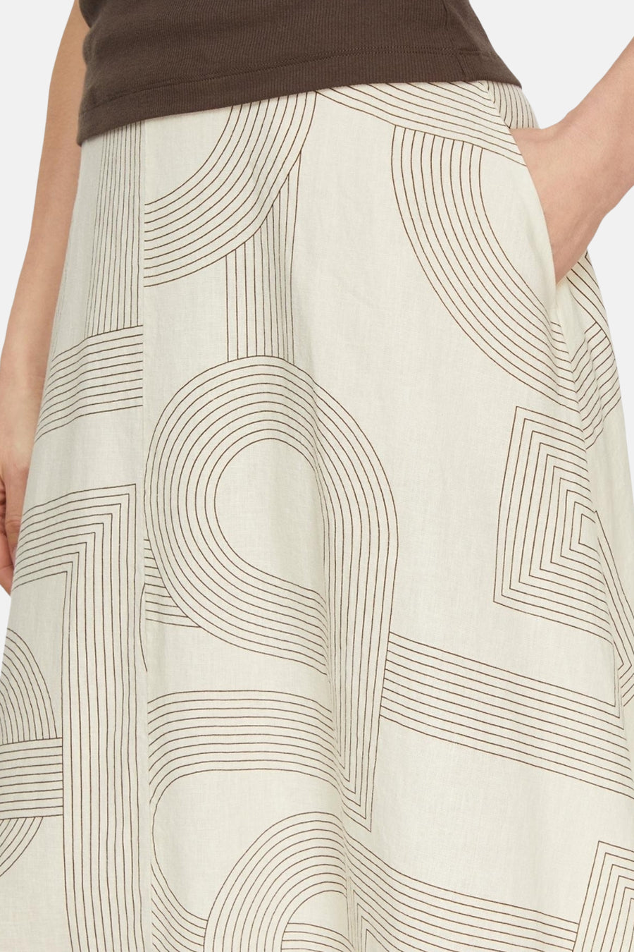 Jupe longue beige de COMMA avec un motif géométrique de lignes marron, une main dans la poche latérale et un top marron.
