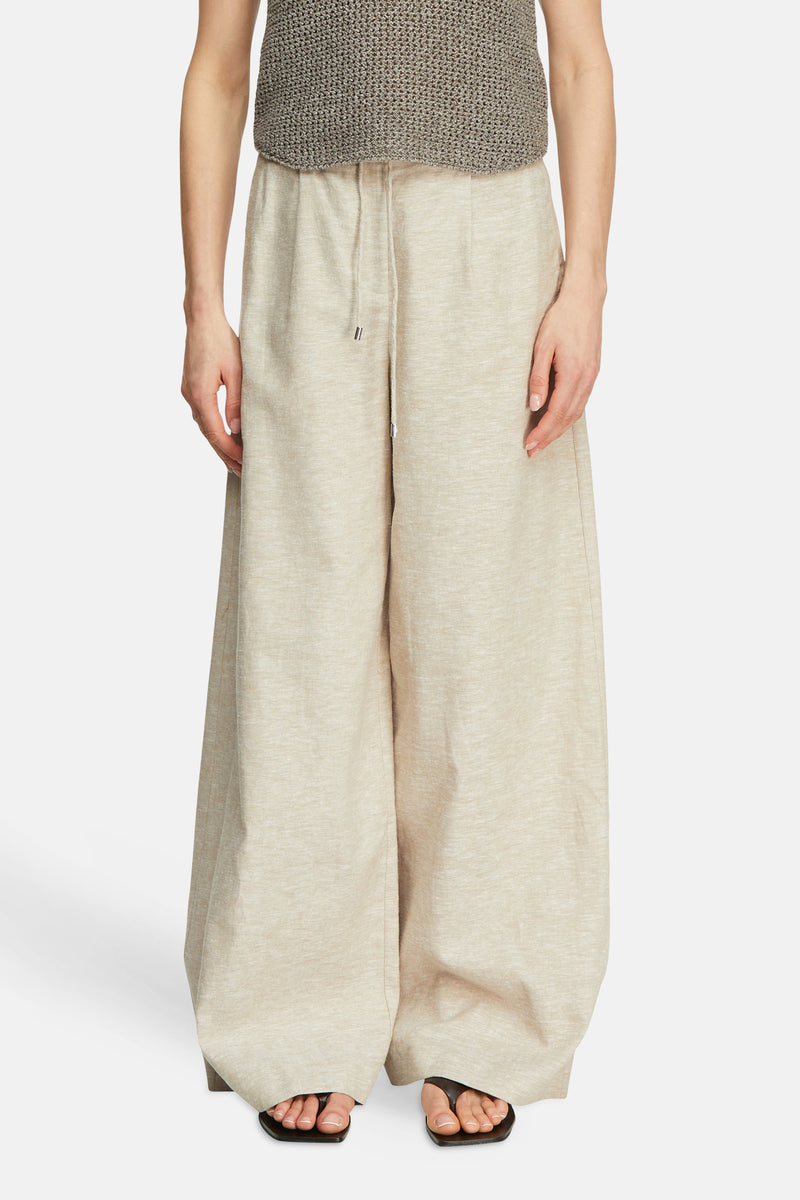 Pantalon de costume taupe de COMMA, à jambes larges et taille à cordon, en tissu chiné, porté avec un haut en maille et des sandales.
