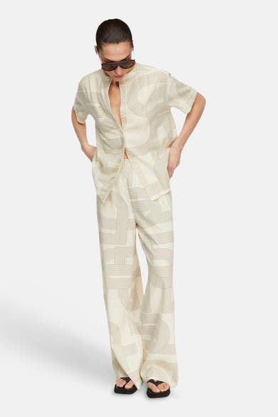 Blouse beige à manches courtes de COMMA à motif géométrique de lignes fines, portée avec un pantalon assorti et des sandales.